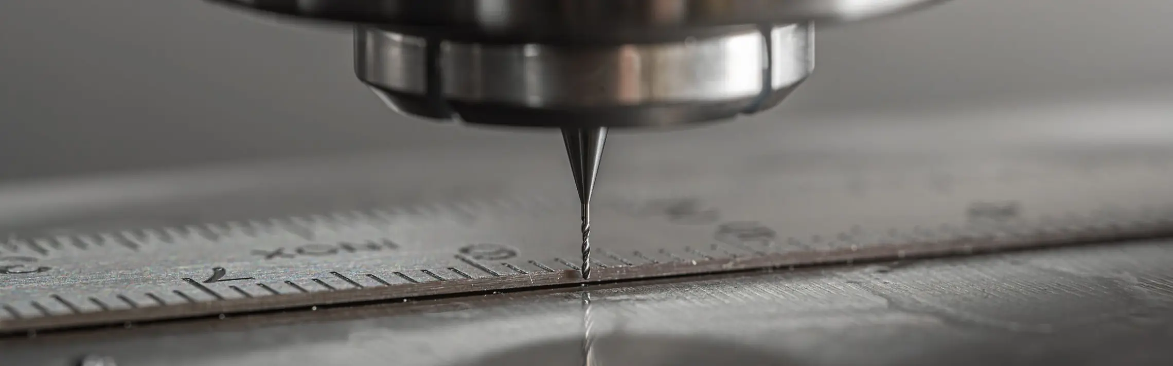 Zbliżenie cienkiego narzędzia obrabiarki CNC tuż nad metalową płytą